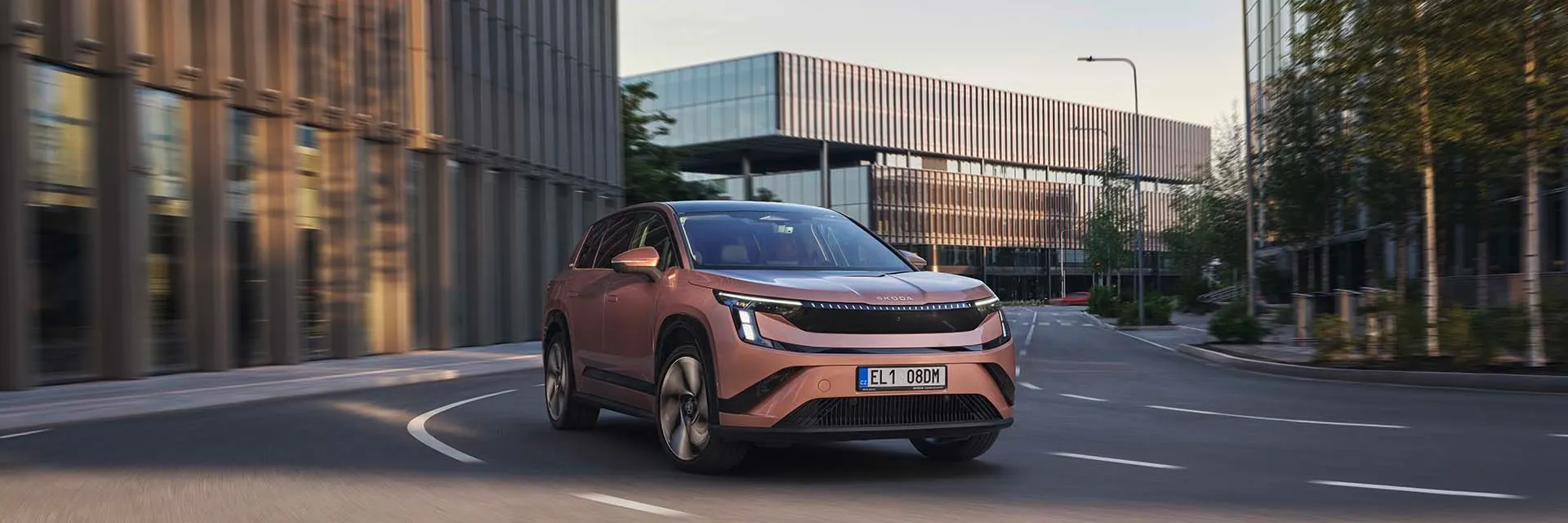 Škoda Peaq pe un drum urban, între clădiri moderne cu fațade din sticlă și metal. 
